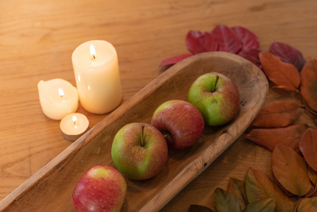 red apple beside two white pillar candles on brown wooden tray